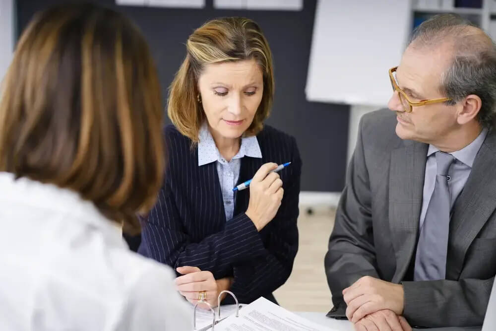 Middle-aged couple planning for retirement in a meeting with a female broker or investment adviser in her office