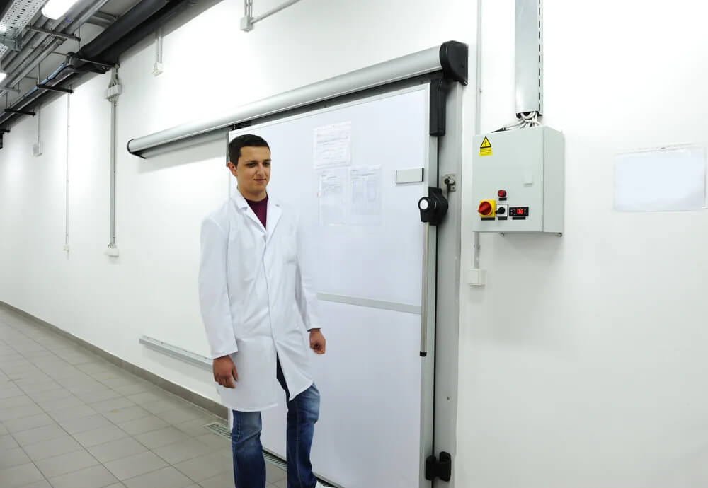 Young worker opening  door of industrial refrigerator